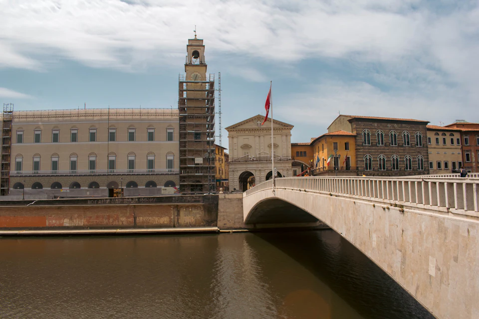 Ponte ad arco su un fiume con palazzi storici e una torre con orologio