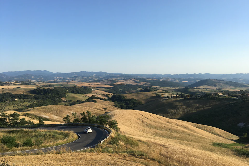 Strada che attraversa le colline toscane con un'auto bianca